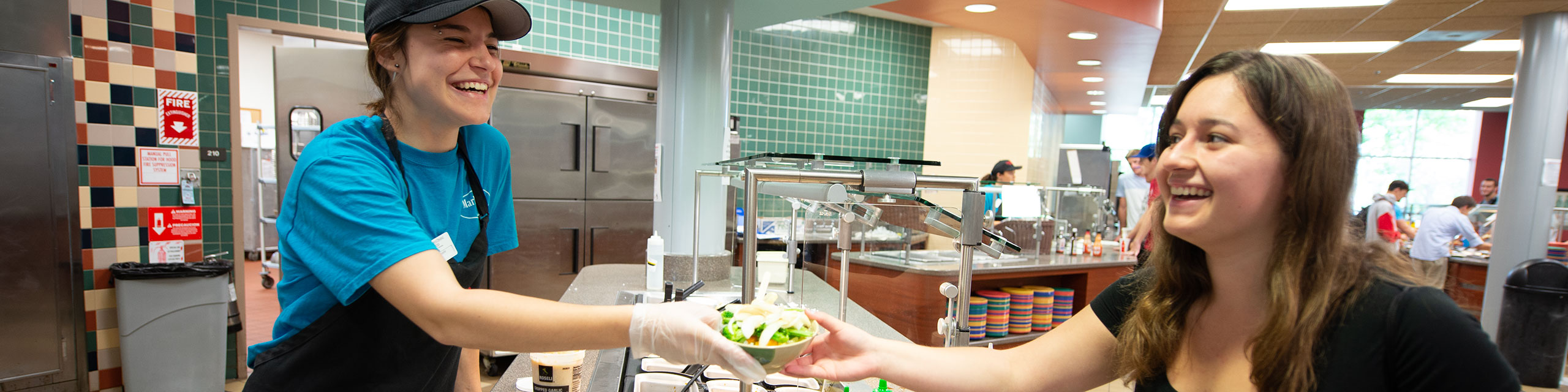 Student worker serves a bowl of food to another student.